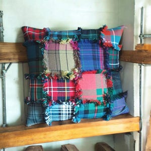 May include: A patchwork pillow with a frayed edge, made from different plaid fabrics in shades of red, blue, green, and brown.