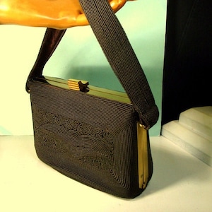 May include: A dark brown woven handbag with a gold clasp and a long strap. The bag has a geometric pattern.