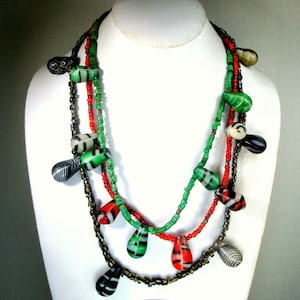May include: A multi-strand necklace with green, red, and black beads. The beads are in the shape of teardrops and have a variety of patterns.