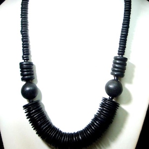 May include: A black necklace, approximately 23 inches long, displayed on a white mannequin. The necklace features a series of small, round, black beads and larger, cylindrical beads. The design includes a large, round bead at the center.