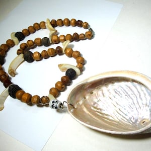 May include: A necklace featuring a large, iridescent abalone shell pendant attached to a strand of brown wooden beads, dark textured beads, white curved shell accents, and a small white bead with a black skull graphic printed on the surface.