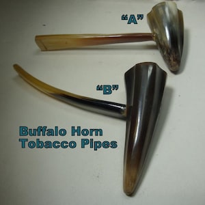 May include: Two tobacco pipes crafted from buffalo horn, labeled A and B. The pipes feature a smooth, polished finish with natural color variations ranging from light tan to dark brown and black. The text Buffalo Horn Tobacco Pipes is visible.