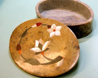 May include: An oval-shaped, brown stone box with a floral design. The lid is open and the inside of the box is empty. The floral design is made of inlaid white and red stones.