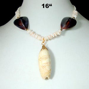 May include: A necklace, 40.6 cm in length, with a cream-colored pendant with brown streaks. It hangs from a strand of small, light-colored shell chips. The design includes two dark heart-shaped beads and gold-colored accents.