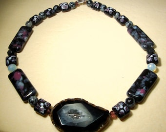 May include: A black and white agate pendant necklace with a silver clasp. The necklace is made with black and white rectangular beads with a floral pattern and clear beads.