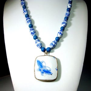 May include: A blue and white porcelain necklace featuring a rectangular pendant with a blue butterfly design. The necklace has a beaded chain with blue and white patterned beads and solid blue beads.