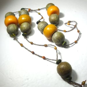 May include: A necklace featuring alternating large, round beads in shades of orange and textured green. The necklace is strung on a delicate, beaded chain with smaller accent beads in orange and brown. The focal point is a large, textured, brown bead.
