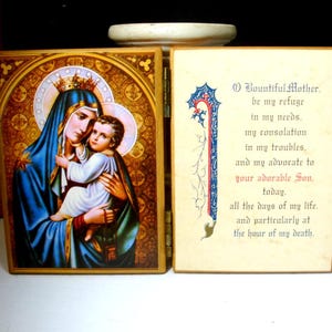May include: A hinged wooden religious icon featuring a depiction of the Virgin Mary holding the Christ Child, with a gold halo and blue robes. The right panel displays a prayer in blue and red script, with the text "O Bountiful Mother."