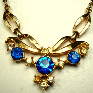 May include: A gold necklace with a bow design and blue and clear rhinestones.