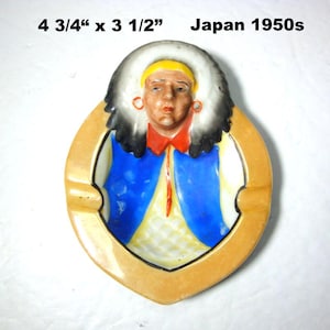 May include: Vintage ashtray from Japan, circa 1950s, measuring 4 3/4" x 3 1/2". The ashtray features a Native American figure with a feathered headdress, red shirt, and blue vest. The ashtray has a tan border.