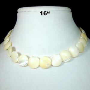 May include: A 16-inch necklace composed of round, off-white, iridescent shell discs. The necklace is displayed on a white mannequin bust against a black background. The shell discs have a natural, pearlescent sheen.