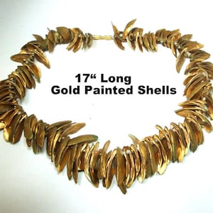 May include: A gold-painted shell necklace, approximately 17 inches long, is displayed against a white background. The necklace is composed of numerous gold-colored shells, arranged in a circular pattern, and connected by a gold clasp.