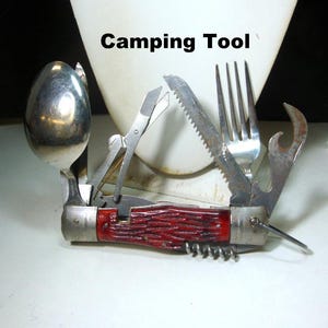 May include: A multi-tool camping tool with a red handle. Features include a spoon, scissors, saw, fork, bottle opener, and corkscrew. The text "Camping Tool" is visible above the tool.