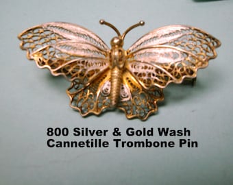 May include: A gold-toned butterfly brooch made of delicate filigree wire. The brooch is labelled "800 Silver & Gold Wash Cannetille Trombone Pin".