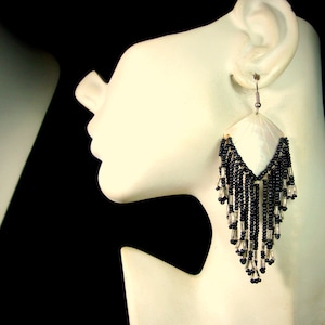 May include: A pair of dangle earrings with a white shell-shaped pendant and black beaded fringe.