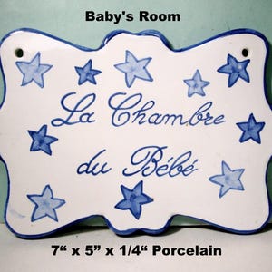 May include: A white porcelain plaque with a blue scalloped edge, measuring 7 inches by 5 inches by 0.25 inches. It features blue hand-painted stars and the French text "La Chambre du Bébé" in blue script, with "Baby's Room" printed above.
