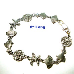 May include: Silver-toned bracelet featuring sea-themed charms, including starfish, seashells, and fish. The bracelet is 8 inches long and has a lobster clasp closure. The charms are connected by small links.