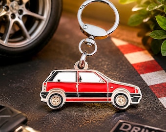 May include: A metal keychain featuring a red and black hatchback car silhouette with silver-toned windows and detailed wheels. The car charm is attached to a circular silver split ring by a small swivel connector, creating a compact automotive accessory.