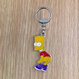 Może przedstawiać: Metalowy brelok do kluczy z Bartem Simpsonem w czerwonej koszulce i niebieskich spodniach, ze spodniami opuszczonymi. Brelok ma srebrny brelok i jest w kolorze żółtym, czerwonym i niebieskim. Projekt jest kreskówkowy.