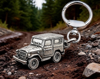 May include: A silver-toned metal keychain featuring a detailed miniature off-road vehicle with a boxy frame, round headlights, a front grille, and rugged tires. The vehicle is attached to a polished circular split ring by a sturdy swivel connector.