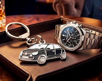 May include: A silver-toned metal keychain featuring a black and white car silhouette charm attached to a circular ring, positioned next to a silver-toned chronograph wristwatch with a black dial and a metallic link bracelet on a brown tray.