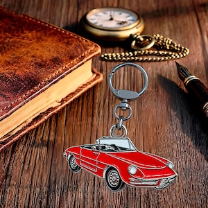 Puede incluir: Un llavero de metal con un dije de coche deportivo descapotable rojo, que incluye una argolla y un cierre de mosquetón plateados. El diseño del coche presenta ruedas negras, un parabrisas blanco y detalles plateados en la carrocería.