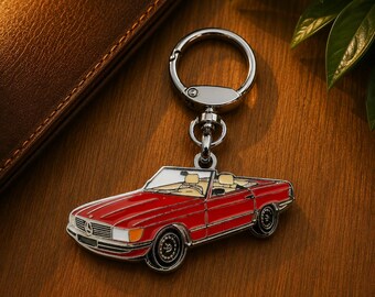 May include: A metal keychain featuring a red convertible car with a tan interior and a silver-toned circular ring attachment. The car design includes white headlights, black wheels, and a prominent silver emblem on the front grille of the vehicle.