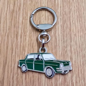 Può includere: Un portachiavi in metallo verde a forma di auto con un anello portachiavi argentato. L'auto è un modello vintage con interni bianchi e dettagli cromati.