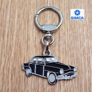 May include: A black metal keychain featuring a vintage Simca car with the Simca logo. The keychain has a silver metal ring.