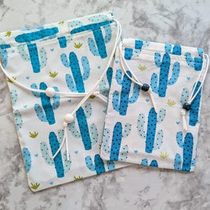 May include: Two white drawstring bags with a blue cactus pattern. The bags have white drawstrings with white beads.