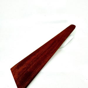 May include: A long, thin, wooden spatula with a reddish-brown color. The spatula is made of a single piece of wood and has a smooth, polished finish.