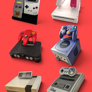 Könnte beinhalten: Eine Sammlung klassischer Nintendo-Spielkonsolen und Handhelds, darunter ein Game Boy mit Spielkassetten, eine weiße Wii mit zwei Controllern, eine schwarze N64 mit rotem Controller, ein violetter GameCube, ein NES und ein Super Nintendo mit Controller.
