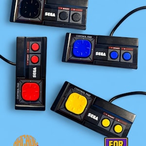 Könnte beinhalten: Vier schwarze Sega-Controller mit Kabeln. Einer hat ein schwarzes Steuerkreuz und Tasten, einer ein rotes, einer ein blaues und einer ein gelbes Steuerkreuz mit passenden Tasten. Der Text lautet ARCADE 1983 und FOR PARTS. Die Controller liegen auf blauem Grund.
