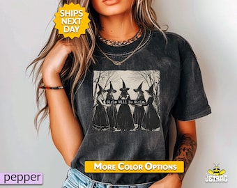 May include: Dark gray t-shirt featuring a graphic of five witches in black dresses and hats, with the text "Girls Will Be Girls." The shirt has a vintage, washed look.