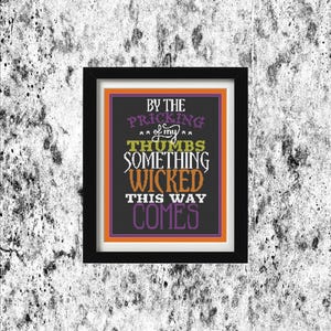 May include: Framed artwork with a black border, featuring the quote "By the pricking of my thumbs, something wicked this way comes." The text is in various colors, including purple, orange, and green, set against a black background. The artwork is displayed on a textured, gray and white wall.