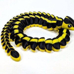 May include: A segmented toy snake in a coiled position. The toy is black with yellow stripes and a yellow head. The snake has a friendly cartoonish design, with small black eyes. The toy is made of plastic.