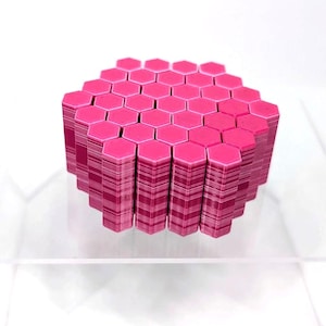 May include: A geometric sculpture composed of stacked, hot pink hexagonal shapes. The edges of the shapes are visible, creating a layered effect. The artwork is displayed on a clear, transparent surface against a white background.