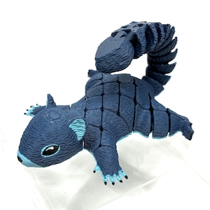 May include: A blue and teal articulated squirrel figurine. The toy squirrel has a segmented body and a curved tail. The squirrel's ears, paws, and the tip of its nose are teal. The eyes are black. The figurine is on a white background.