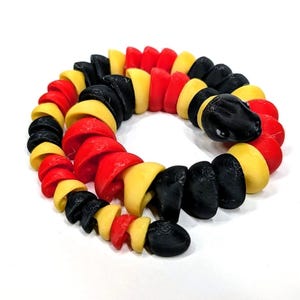 May include: A colorful, articulated snake toy in red, yellow, and black. The snake is coiled and has a detailed head. The segments are rounded and connected, allowing for flexible movement. The toy is made of plastic.