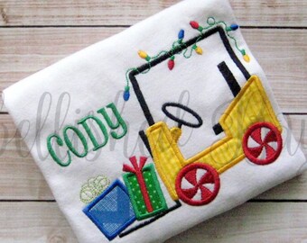 May include: A white t-shirt with a yellow toy truck carrying presents and Christmas lights. The name "Cody" is embroidered on the shirt.