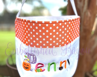 May include: White Halloween trick-or-treat bag with an orange and white polka dot top. The bag has the name "Penny" embroidered on the front in colorful letters with Halloween-themed embellishments.