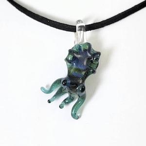 May include: A glass octopus pendant with a dark blue and green color scheme. The pendant is hanging from a black cord.