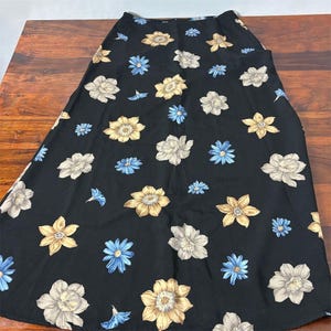 May include: A black skirt with a floral pattern. The skirt features a repeating pattern of white, yellow, and blue flowers. The skirt is made of a lightweight fabric and has a flowing silhouette. The skirt is suitable for casual wear.