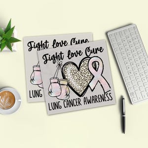 a desk with various items, including a keyboard, a cup of coffee, and a plant. There are two pieces of paper with a pink ribbon and leopard print design, along with the text "Fight love Cure Lung Cancer Awareness".