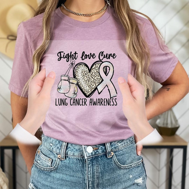 A person wearing a pink t-shirt with a graphic design related to lung cancer awareness, including a heart, boxing gloves, and a pink ribbon.