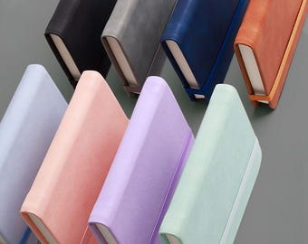 May include: A collection of eight rectangular notebooks arranged in two rows, featuring covers in black, gray, blue, orange, light blue, pink, purple, and mint green. Each notebook is secured with a matching elastic band and has white pages.