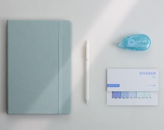 May include: A light blue notebook with an elastic band, a white pen, a blue dot liner, and a pack of sticky notes with blue and purple tabs. The word "STICKER" is printed on the sticky notes.