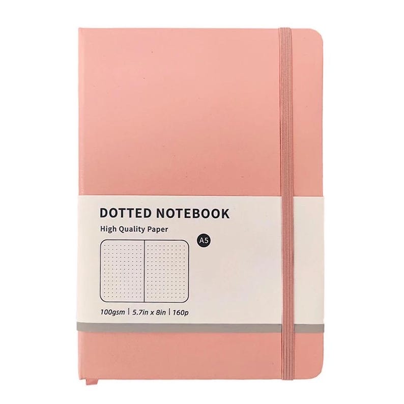 May include: A pink A5 dotted notebook with a matching elastic band closure. The notebook has a white label with the text "Dotted Notebook" and "High Quality Paper". The label also includes the measurements: 5.7in x 8in.