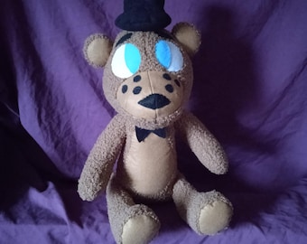 Op de afbeelding: Een bruine pluche teddybeer met een zwarte hoed en een zwarte strik. De beer heeft blauwe ogen en een zwarte neus.