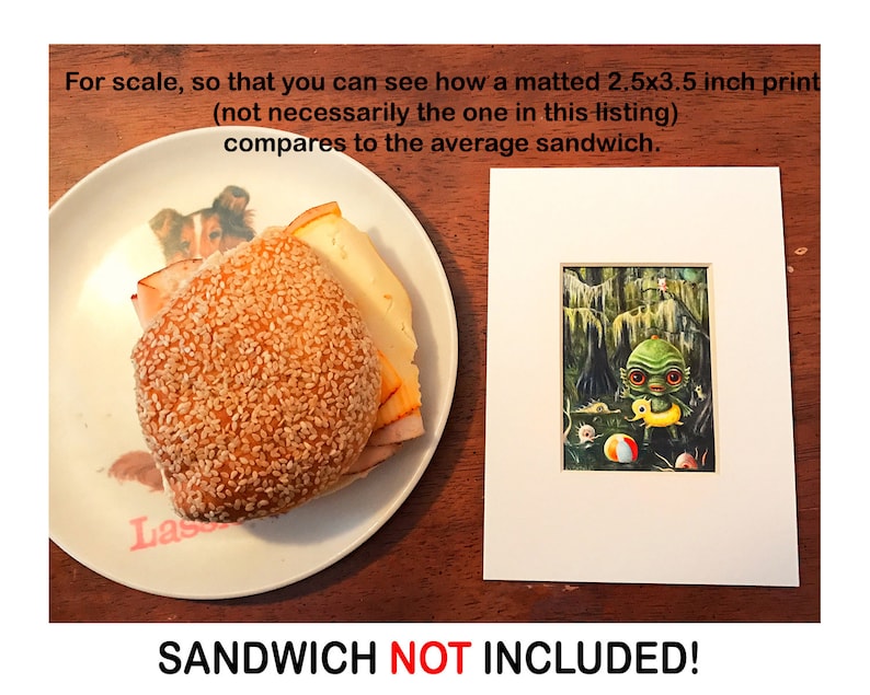 May include: A white matted print of a green creature holding a yellow float in a swamp. The print is 2.5 by 3.5 inches. A sandwich on a plate is shown for scale. The text "SANDWICH NOT INCLUDED!" is printed below the image.